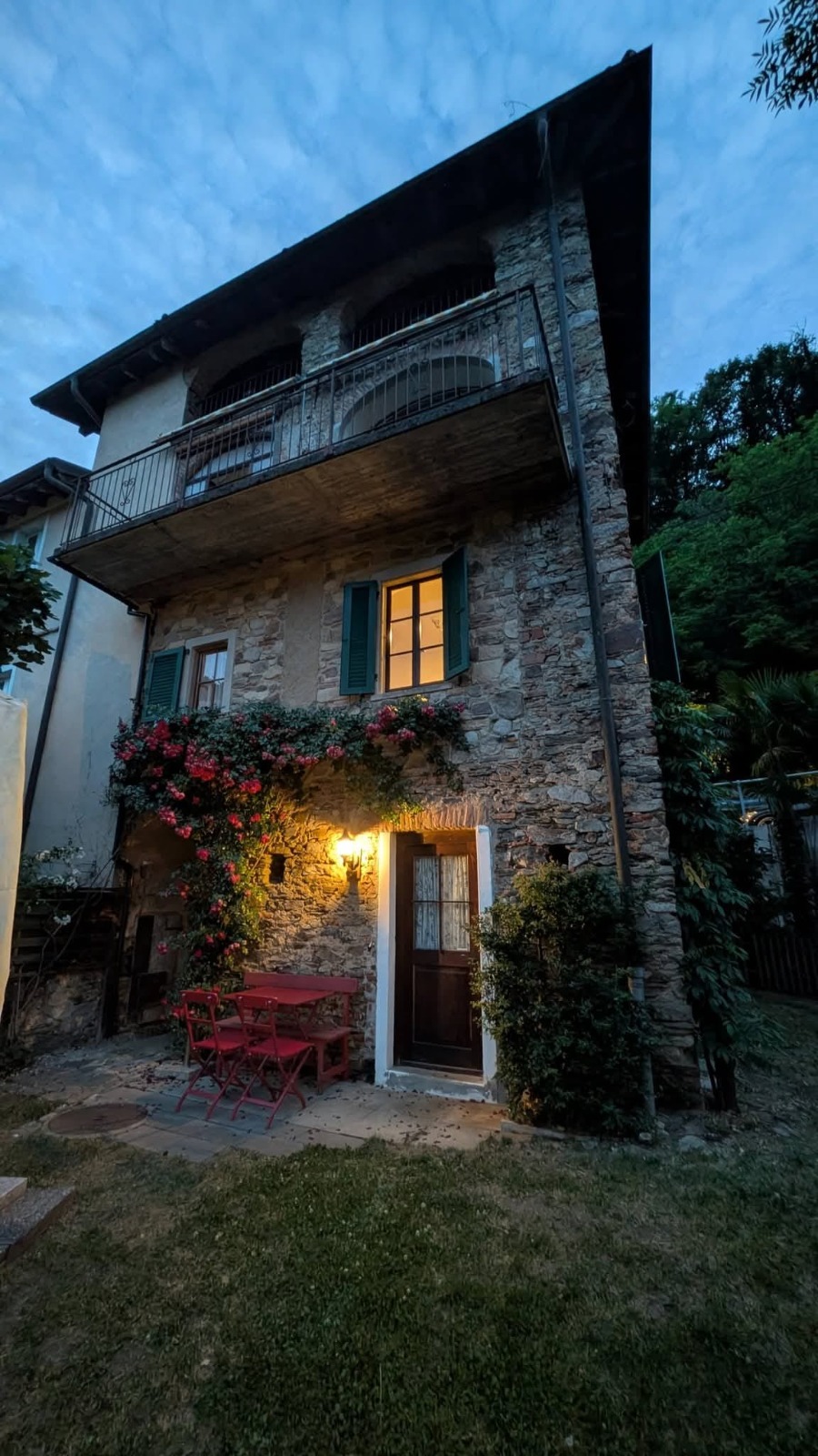 Gartenseite der Casa Edera am Abend mit blühenden Rosen und rotem Bistrotisch